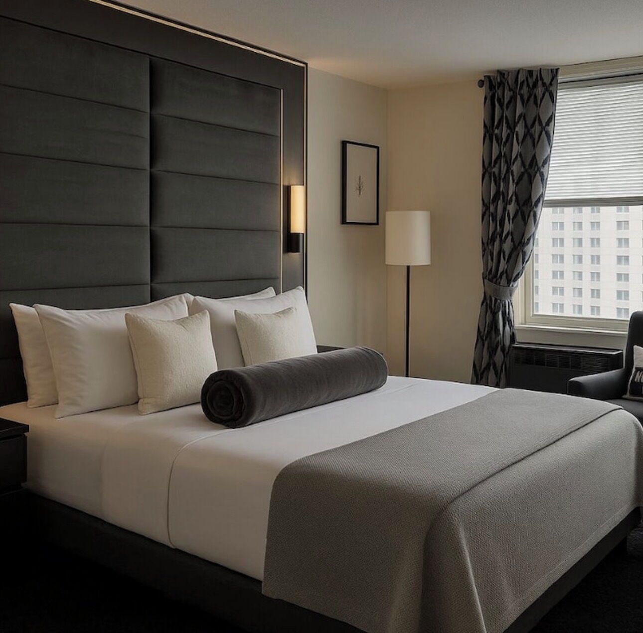 A hotel room with a large bed, a headboard, a nightstand, a lamp, a chair, and a window with curtains.