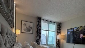 Une chambre d’hôtel avec un lit, une télévision, une fenêtre avec des rideaux et un tableau encadré au mur.