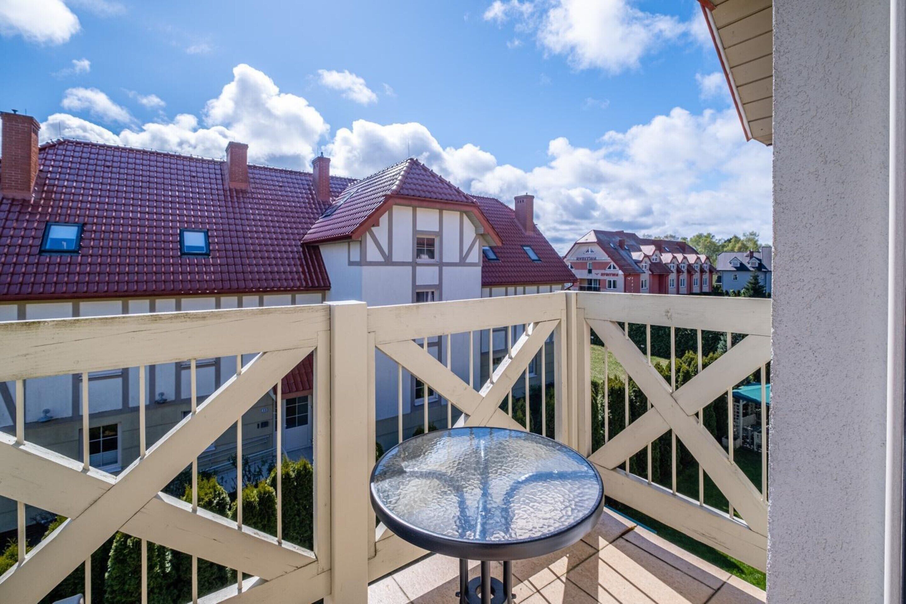 A balcony with a glass table, a white railing, and houses with red roofs in the background.