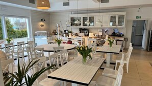 A modern kitchen with white cabinets, a dining area with white tables and chairs, and a view of the outdoors. - Luxury Apartment for 6 People, With a Bathtub (Krokowa)