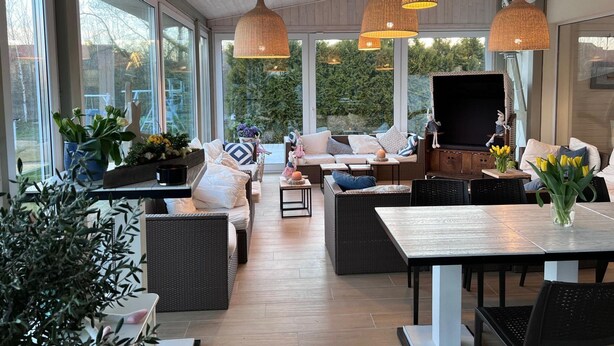 A spacious indoor area with large windows, wicker furniture, and hanging pendant lights. - Luxury Apartment for 6 People, With a Bathtub (Krokowa)