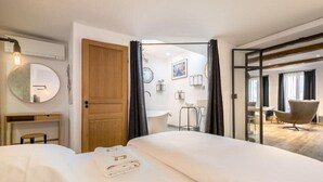 Ett hotellrum med en säng, ett skrivbord, en spegel, ett badrum och utsikt över vardagsrummet.
