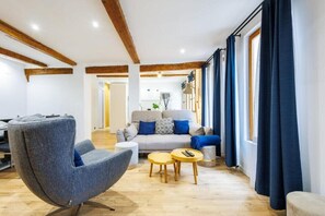 Ein modernes Wohnzimmer mit einem grauen Sessel, einer blauen Sofakissen-gepolsterten Couch, einem Holztisch und einem großen Fenster mit dunklen Vorhängen.