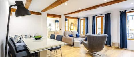 A modern living room with a dining area, wooden beams, a sofa, a chair, and a lamp.