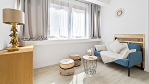 Een moderne woonkamer met een blauwe bank, een houten hoofdbord, een lamp, twee voetenbankjes en een ronde salontafel.