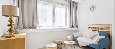 A modern living room with a blue sofa, a wooden headboard, a lamp, two ottomans, and a round coffee table.