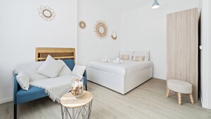 Een slaapkamer met een blauwe bank, een wit bed, een klein krukje en decoratieve wandkunst.
