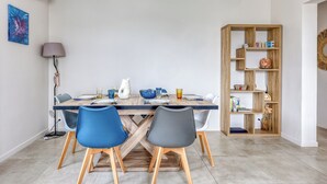 Un coin repas avec une table en bois, des chaises bleues et grises, et une bibliothèque en bois agrémentée d’objets décoratifs.