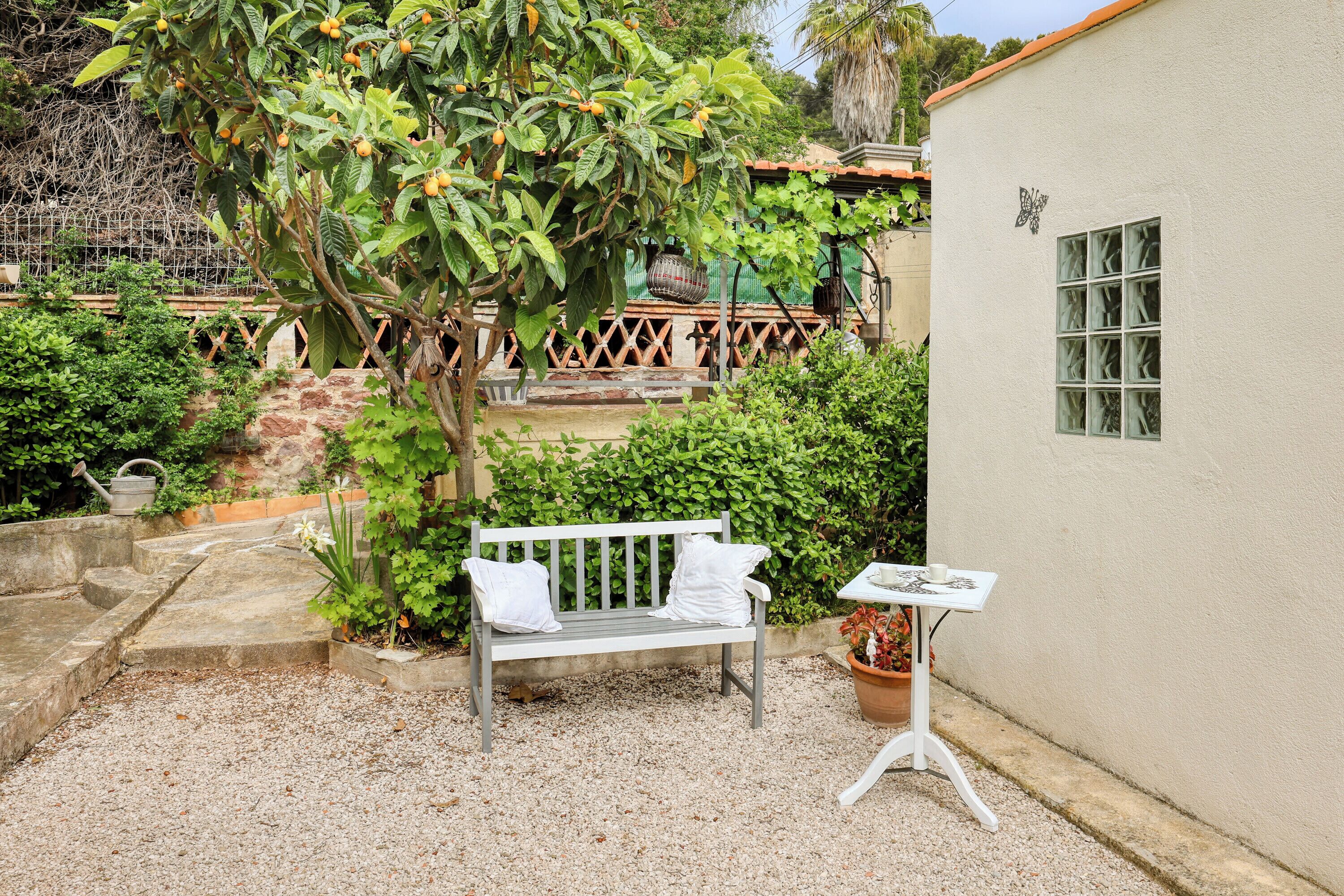 A garden with a bench, a table, and a white building with a window.
