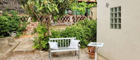 A garden with a bench, a table, and a white building with a window.