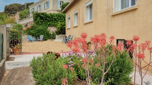 Un immeuble résidentiel doté d’un jardin, d’un espace extérieur aménagé pour s’asseoir et d’un escalier menant à l’entrée.