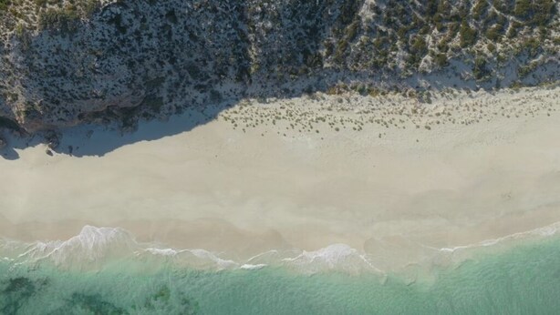 Une plage avec une eau claire, un rivage sablonneux et une zone rocheuse.