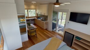 Une chambre compacte comprenant un lit, une petite kitchenette, un téléviseur et une porte coulissante donnant sur un balcon.