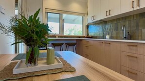Une cuisine moderne avec des meubles en bois, une grande fenêtre et un îlot central agrémenté d’un vase et d’une bougie.