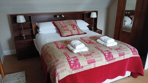 A neatly made bed with a red and beige patterned bedspread, two white pillows, and two folded white towels.