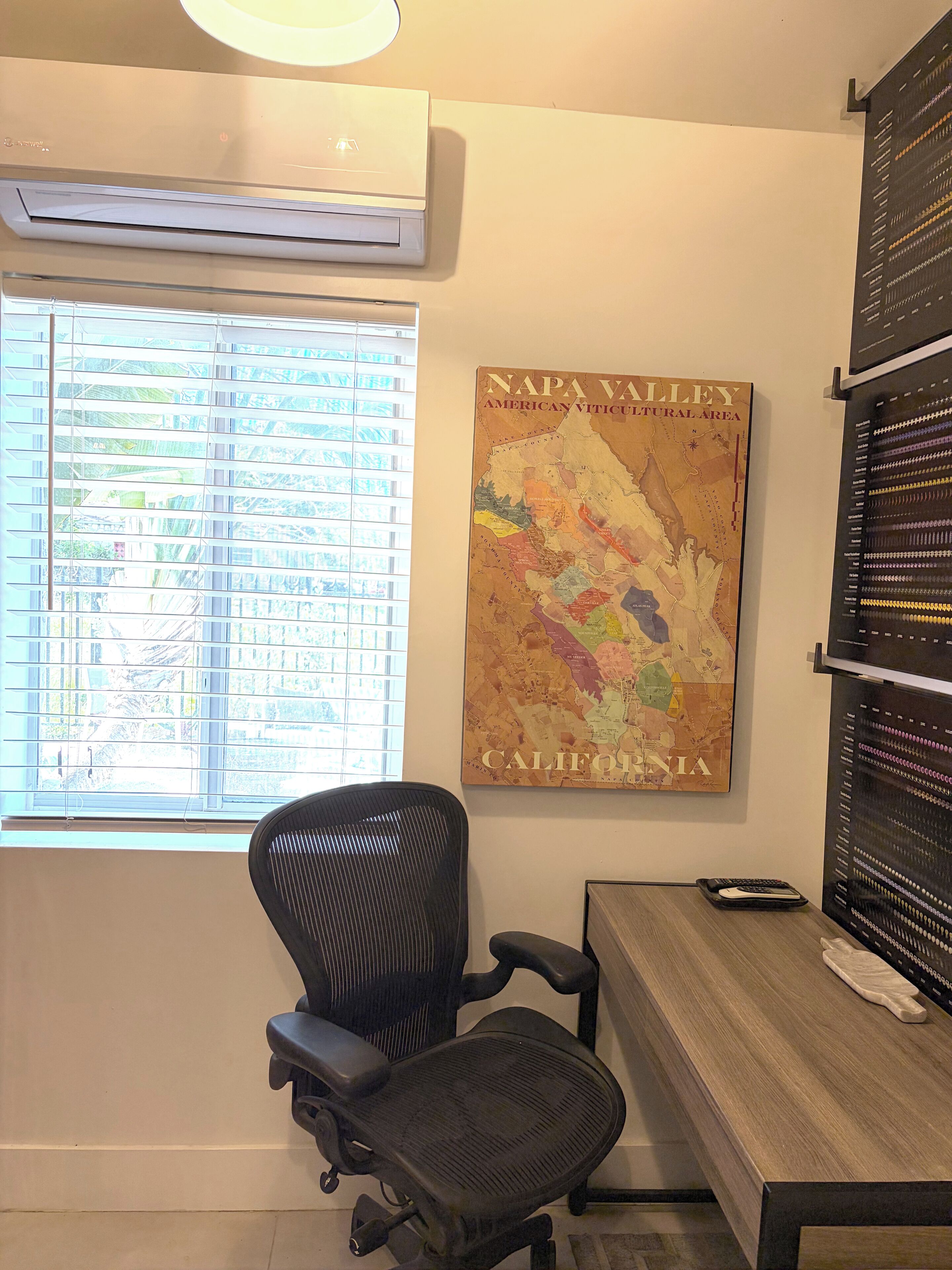 Una habitación con ventana, aire acondicionado, un mapa del Valle de Napa, una silla de oficina negra y un escritorio de madera.