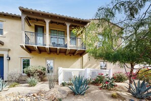 A two-story building with a balcony, a white fence, and various desert plants. - Casa Gregario - Beautiful Condo in Spanish Walk Neighborhood (Palm Desert)