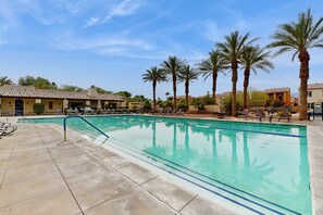 Ein Swimmingpool mit klarem, blauem Wasser, umgeben von Palmen und Liegestühlen.