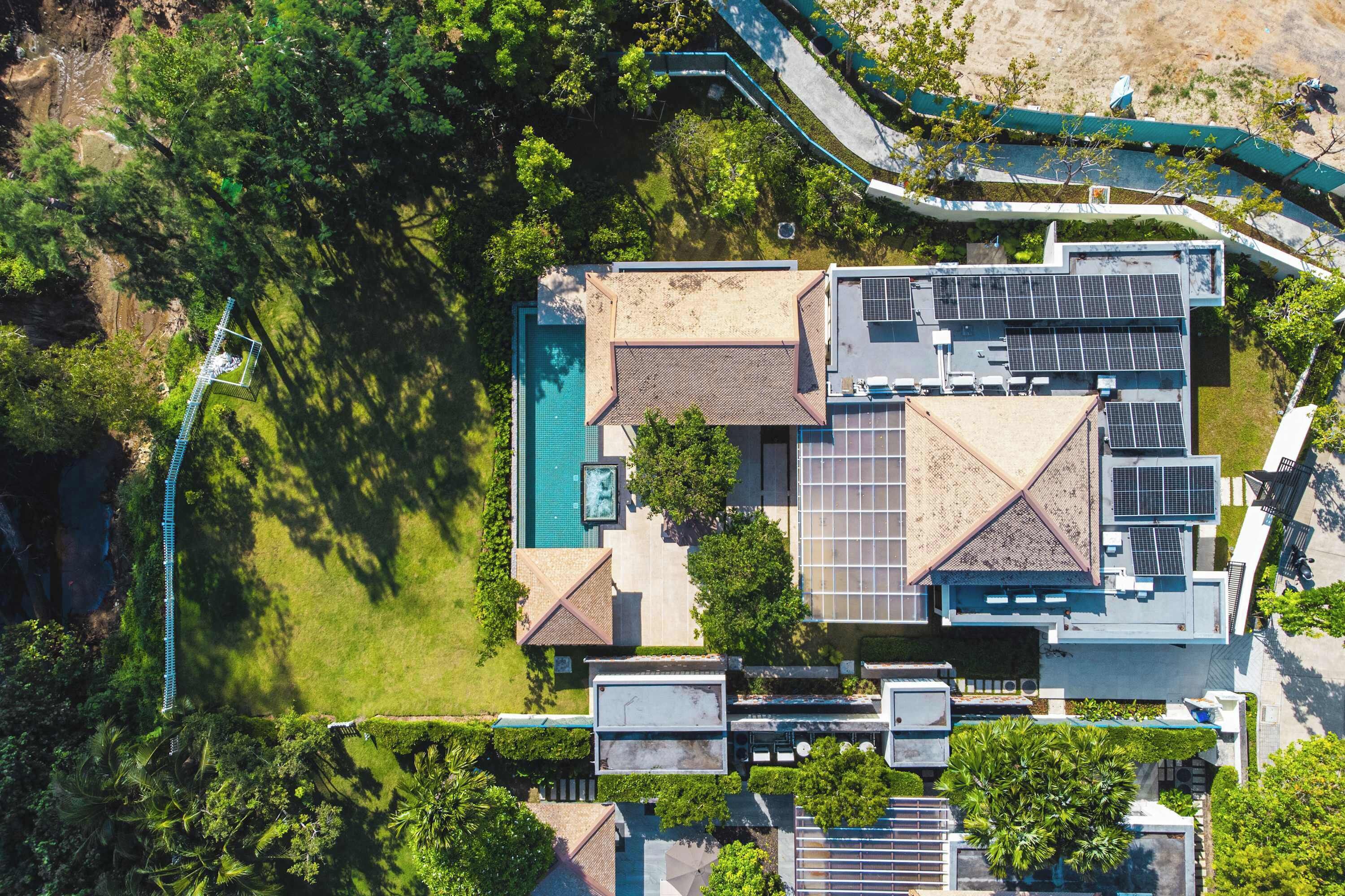An aerial view of a hotel with a swimming pool, solar panels, and a bridge connecting different sections.