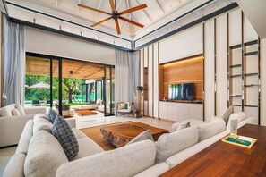 A spacious living area with a large sofa, a wooden coffee table, and a ceiling fan. - Banyan Tree Grand Residences by Banyan Living (Choeng Thale)