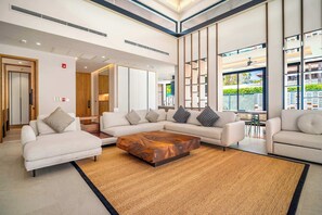 A modern hotel lobby with a sectional sofa, a wooden coffee table, and large windows offering a view of the outdoors. - Banyan Tree Grand Residences by Banyan Living (Choeng Thale)