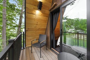 A wooden deck with a chair and a table, a balcony door, and a view of trees. - Lakefront A-Frame | Hot Tub, Dock & Views | Seneca Lake (Penn Yan)