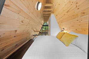 A wooden cabin interior with a bed, a nightstand, and a window. - Lakefront A-Frame | Hot Tub, Dock & Views | Seneca Lake (Penn Yan)