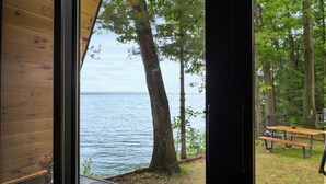 A wooden cabin with a view of a lake and a picnic table. - Lakefront A-Frame | Hot Tub, Dock & Views | Seneca Lake (Penn Yan)