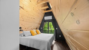 A bedroom with a wooden ceiling, a bed with white and yellow bedding, and a window with curtains. - Lakefront A-Frame | Hot Tub, Dock & Views | Seneca Lake (Penn Yan)