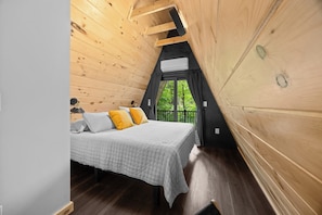 Een slaapkamer in een houten hutje, met een bed, kussens, een raam en een airconditioning.