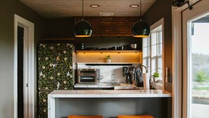 Una cocina con una isla central, dos taburetes de bar, horno empotrado e iluminación colgante.
