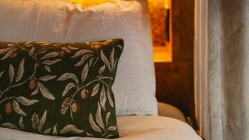 Une chambre confortable avec un plafond en pente, un lit recouvert de draps blancs, un coussin à motifs verts et une vue sur une forêt par la fenêtre.