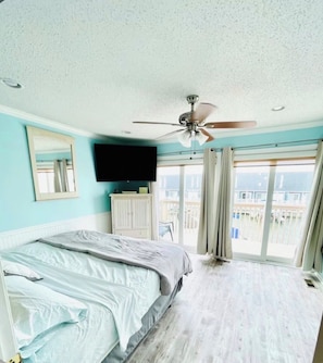 Ein Schlafzimmer mit einem Bett, Deckenventilator, Fernseher, einem Fenster mit Vorhängen und Meerblick.