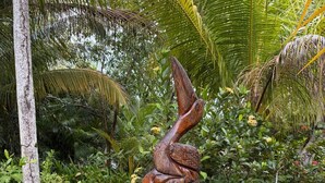 Eine Skulptur einer Hand, die eine Schlange hält, in einem Garten mit verschiedenen tropischen Pflanzen.