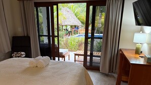 Ein Hotelzimmer mit Bett, Schreibtisch, Fernseher und Blick auf Pool und Palmen.