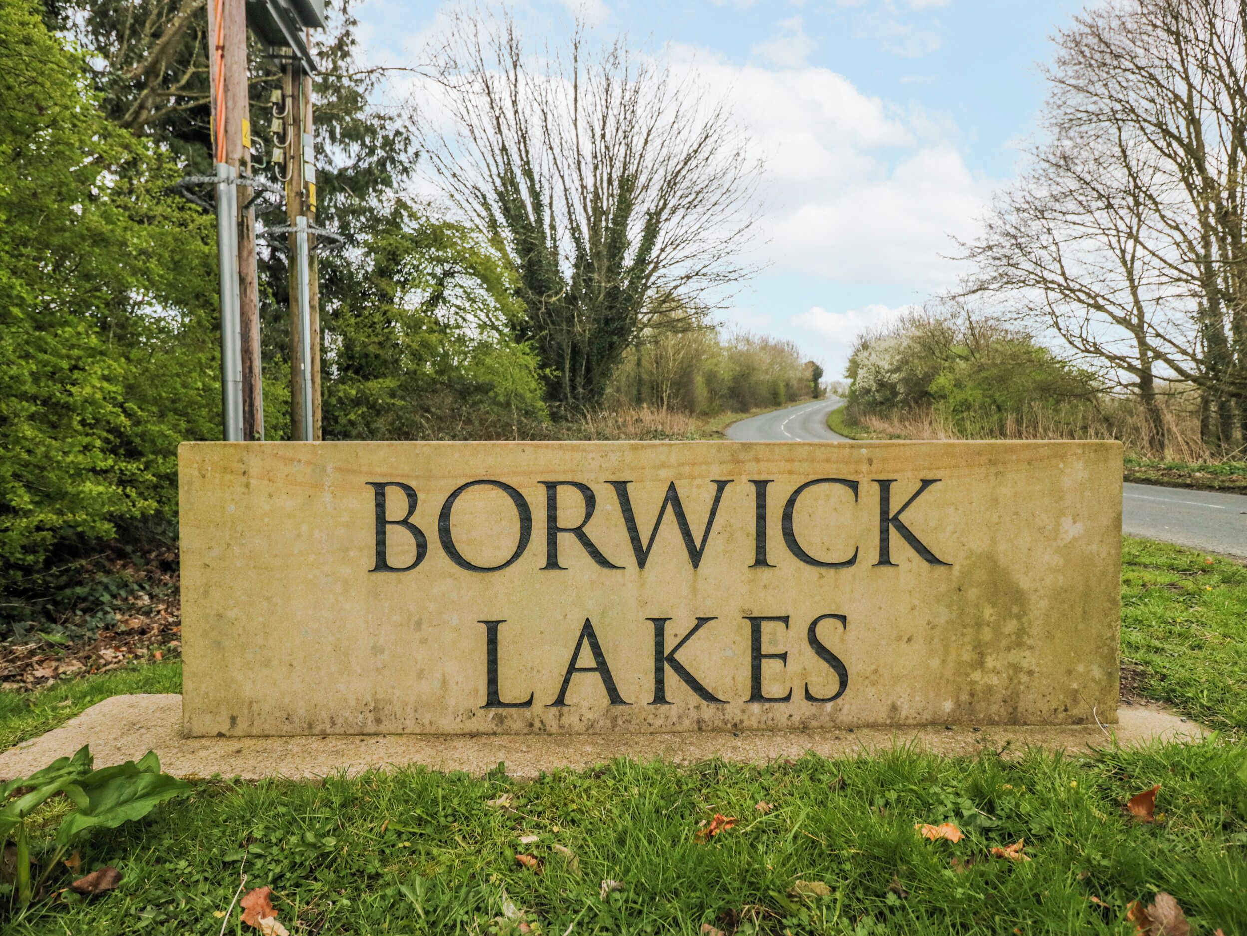 A sign for Borwick Lakes with a road in the background.