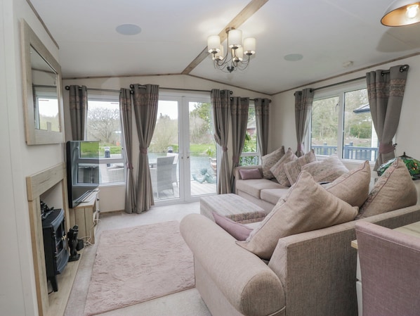 A living room with a sofa, a television, a fireplace, and a view of the outdoors. - Carp Lodge (Carnforth)