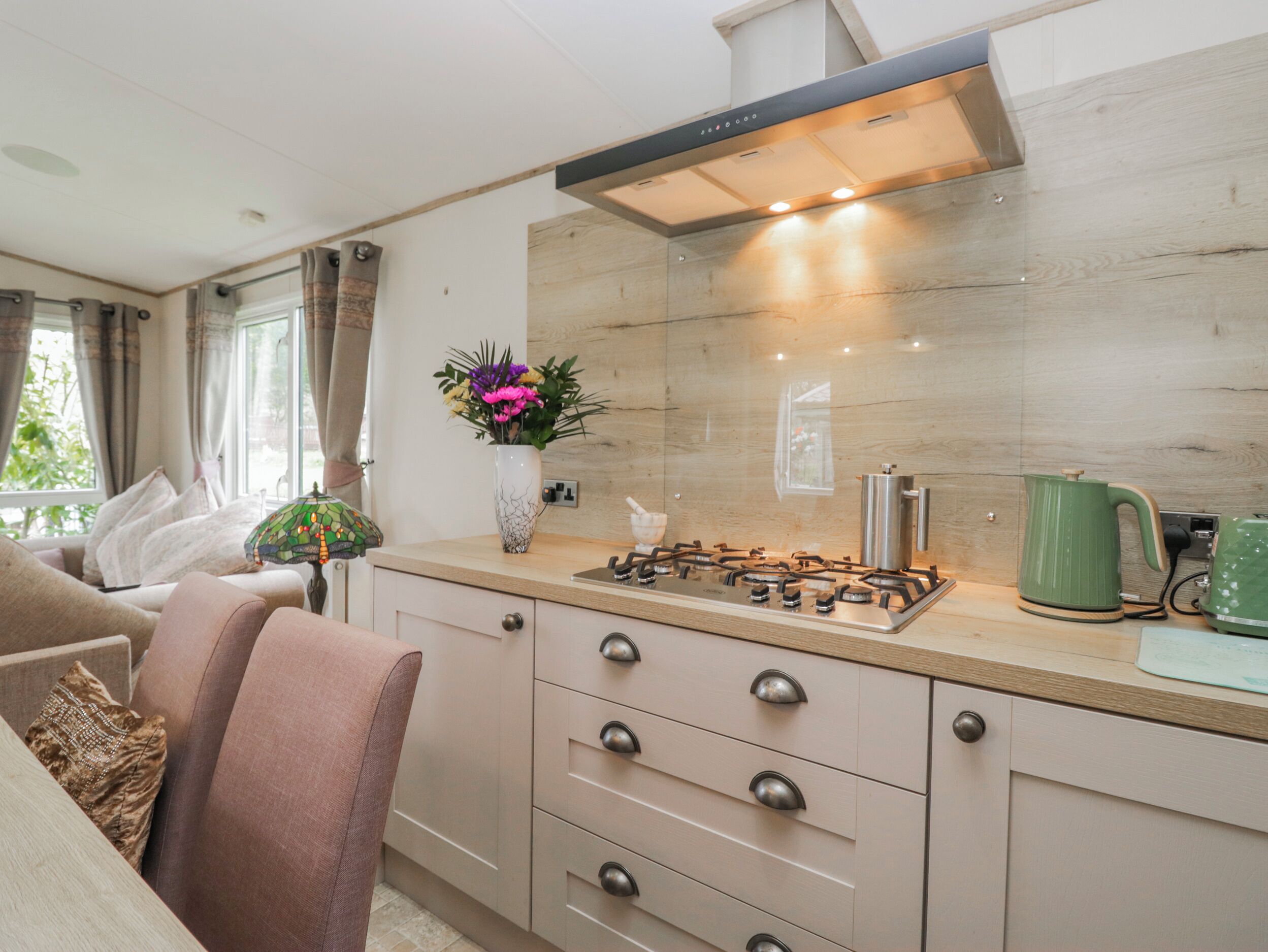 A modern kitchen with a gas stove, a green kettle, and a vase with flowers on the counter.