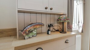 A room with a wooden dresser, a fish sculpture, a stained glass lamp, and a window with curtains. - Carp Lodge (Carnforth)