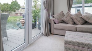 A room with a sliding glass door leading to a patio, a sofa with patterned cushions, and a wicker chair. - Carp Lodge (Carnforth)