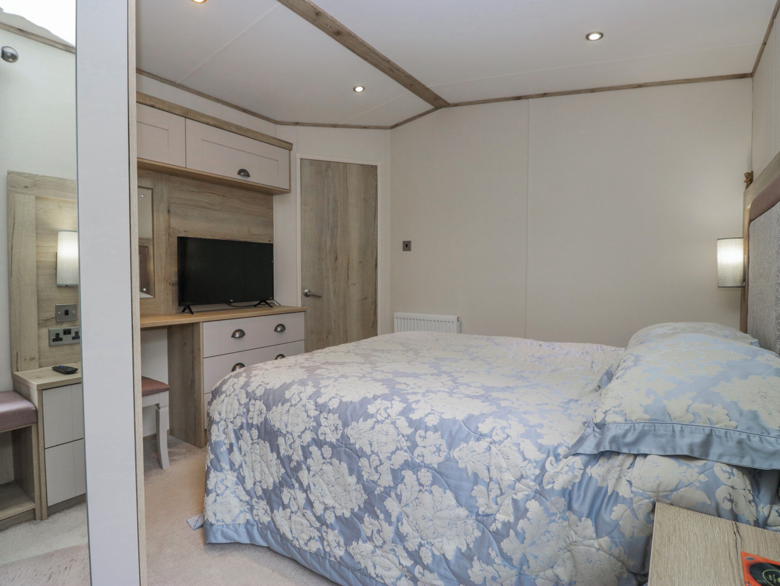 Quarto com cama, escrivaninha, televisão e guarda-roupa.