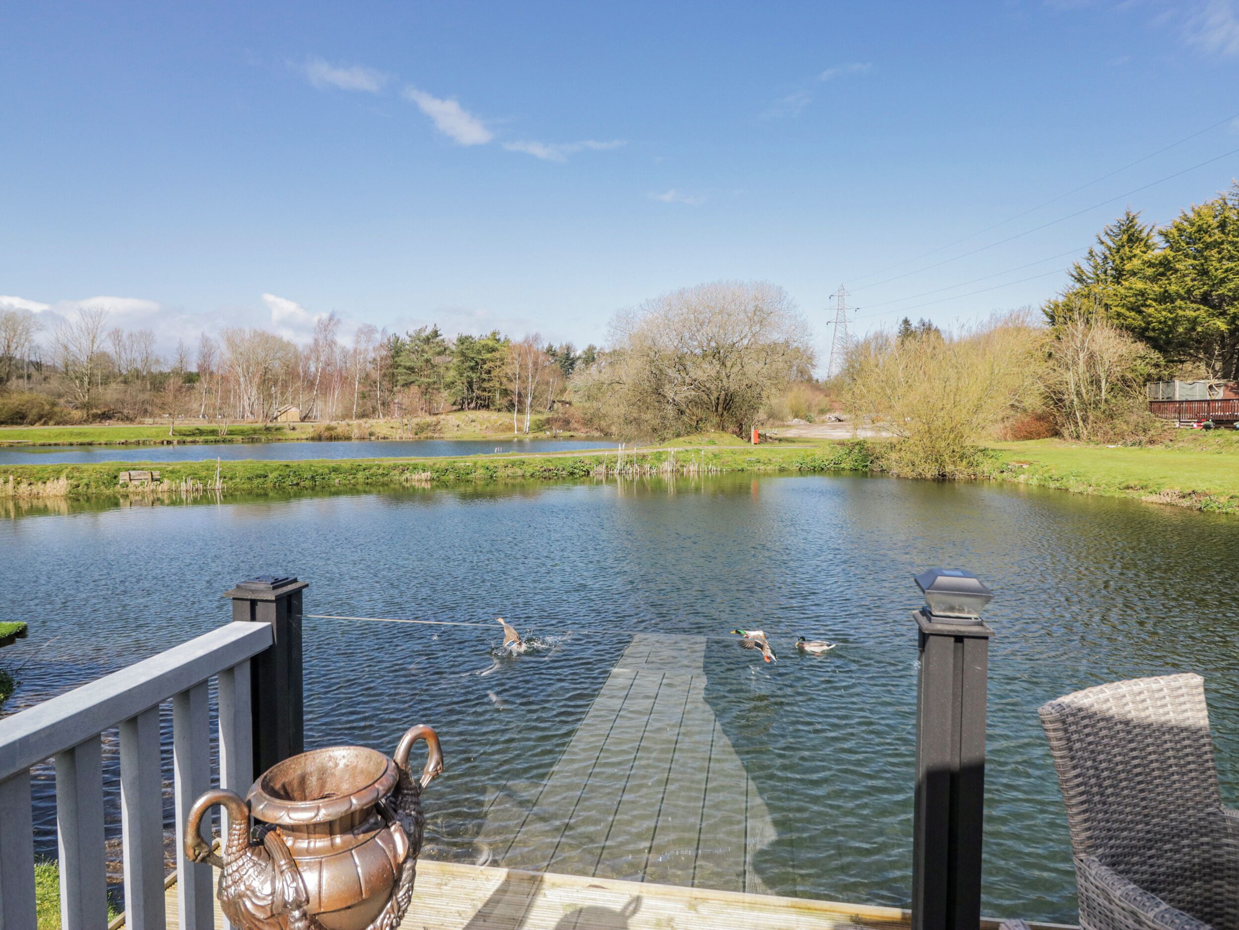 A calm pond with ducks, a wooden deck, and a metal birdbath.
