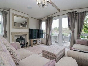A living room with a television, sofa, ottoman, and a view of the outdoors. - Carp Lodge (Carnforth)