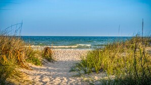 Un sentier qui longe la plage et mène à l’océan, sous un ciel dégagé.