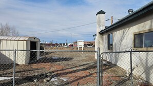 Un espace extérieur clos, comprenant un bâtiment, un abri de jardin et une surface pavée.