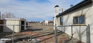 A fenced outdoor area with a building, a shed, and a paved ground.