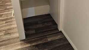A room with a wooden floor, a white wall, and a clothing rack.
