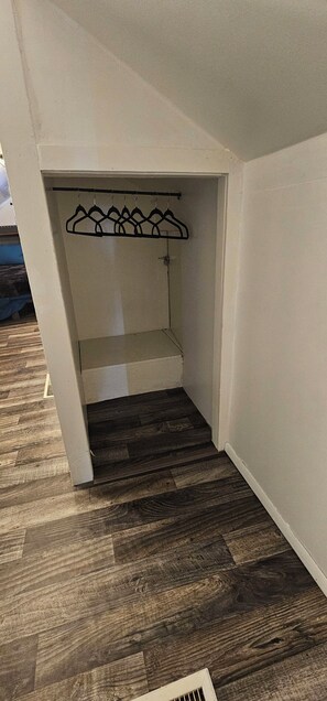 A room with a wooden floor, a white wall, and a clothing rack. - Downtown home family and pets. (Alamosa)