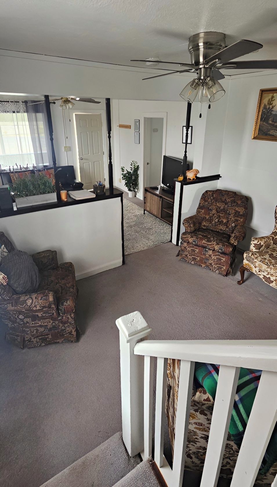 Un salon doté d’un ventilateur de plafond, d’un fauteuil à motifs, d’un canapé et d’un escalier menant à un autre niveau.