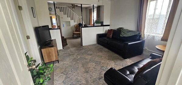 Een woonkamer met een bank, een televisie en een trap naar een verdieping erboven.
